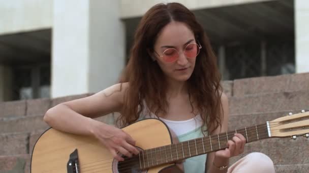 Mujer tocando la guitarra acústica en las escaleras
 - Metraje, vídeo