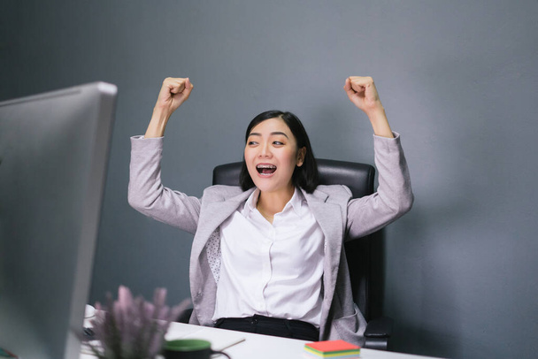 feliz asiático negocios mujer en su oficina escritorio trabajando en su computer.Happy mujer trabajadora con excitada cara reacción
. - Foto, imagen