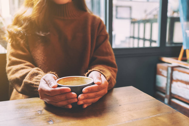 Κοντινό πλάνο εικόνα μιας γυναίκας που κρατά ένα φλιτζάνι ζεστό καφέ στο ξύλινο τραπέζι - Φωτογραφία, εικόνα