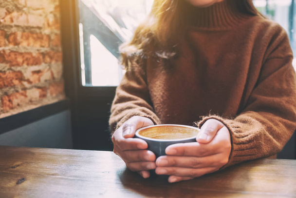 Крупним планом зображення жінки, що тримає чашку гарячої кави на дерев'яному столі
 - Фото, зображення