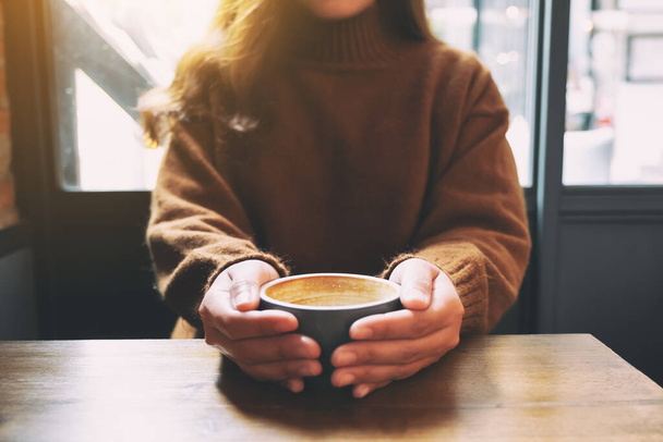 Closeup image of a woman holding a cup of hot coffee on wooden table - Photo, Image