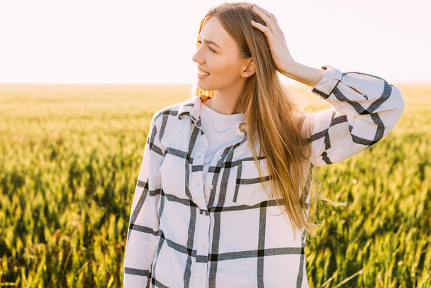 A happy beautiful woman in a wheat field admires the beauty of the fields against the background of the sunset - 写真・画像