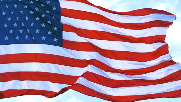 Großaufnahme einer großen amerikanischen Flagge, die vor blauem Himmel und weißen Wolken weht. US-Flagge - amerikanische Flagge weht im Wind. USA-Flagge am strahlend blauen Himmel. Offizielle Flagge der Vereinigten Staaten von Amerika. - Foto, Bild
