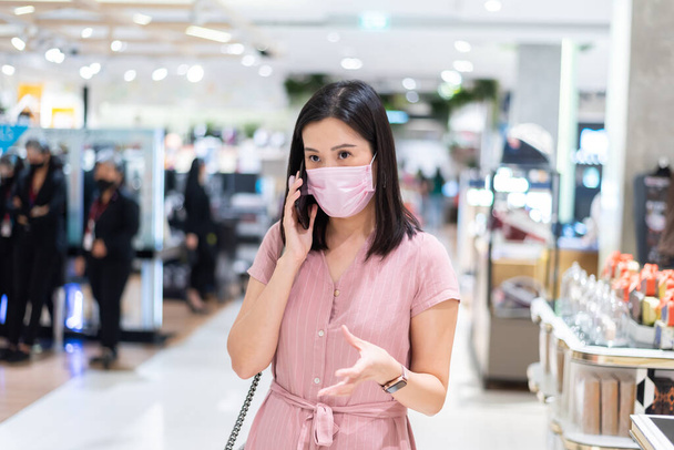 Азиатская женщина разговаривает и делает покупки в торговом центре после открытия изоляции с розовой маской и социальной дистанцированности
. - Фото, изображение
