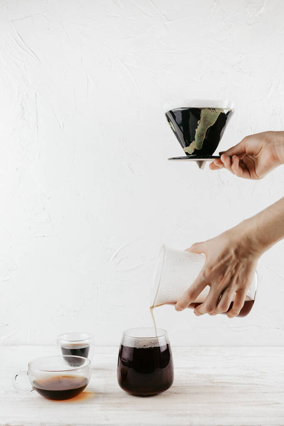 Woman's hands holding coffee dripper and pouring in glass three glass cups on wooden background - Foto, afbeelding