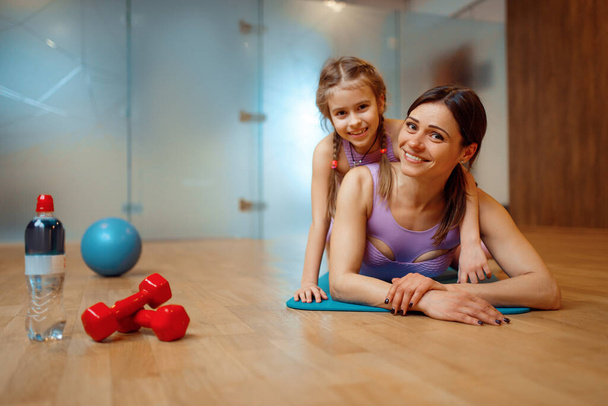 Mother and daughter lying on mat together in gym, fitness workout, gymnastic. Mom and little girl in sportswear, joint training in sport club - Photo, Image