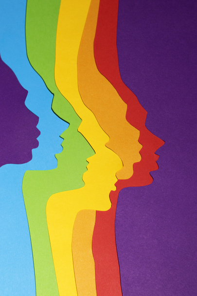 De genderneutrale regenboogkleurige profielen zijn uit papier gesneden. De verticale papieren kunstfoto is gemaakt op een paarse achtergrond. Er is een plaats voor tekst.. - Foto, afbeelding