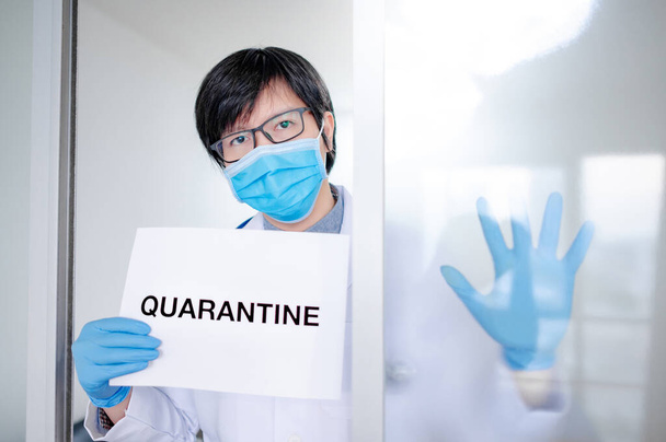 Male Asian Doctor or Physician man wearing surgical mask and latex gloves showing paper with message Quarantine in hospital clinic. Quarantine campaign during Coronavirus (COVID-19) pandemic - Фото, зображення