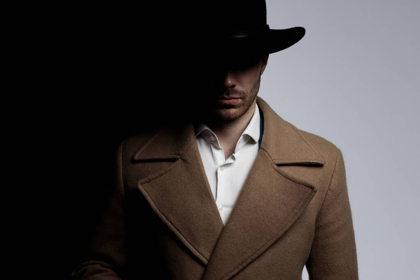 misterioso giovane ragazzo in cappotto lungo indossa cappello e posa in ombra su sfondo grigio nero
 - Foto, immagini