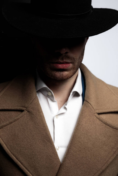 μυστηριώδες μοντέλο μόδας σε μακρύ παλτό ποζάρουν σε σκιά σε μαύρο γκρι φόντο - Φωτογραφία, εικόνα