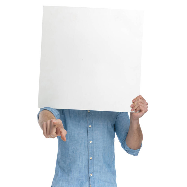Yüzü boş tahtayla kaplanmış genç bir adam, beyaz arka planda izole edilmiş bir parmak ve ayakta duruyor, portre. - Fotoğraf, Görsel