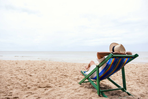 Μια γυναίκα ξαπλωμένη σε μια καρέκλα παραλίας με αίσθημα χαλάρωσης - Φωτογραφία, εικόνα