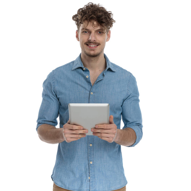 χαμογελαστός casual τύπος σε denim πουκάμισο κρατώντας καρτέλα και στέκεται απομονωμένο σε λευκό φόντο, πορτρέτο - Φωτογραφία, εικόνα