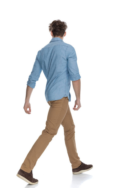 Beyaz arka planda, tam vücut, yalıtılmış bir şekilde yürümeye çalışan kot gömlekli genç bir manken. - Fotoğraf, Görsel