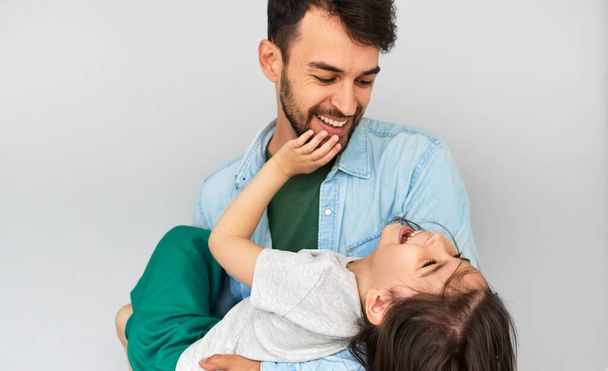 Studio horizontal image of a loving father embraces his cute daughter in his arms. Happy daddy and his little girl playing, cuddling, and enjoying time together on Father's Day. Childhood and fatherhood concept. - Φωτογραφία, εικόνα
