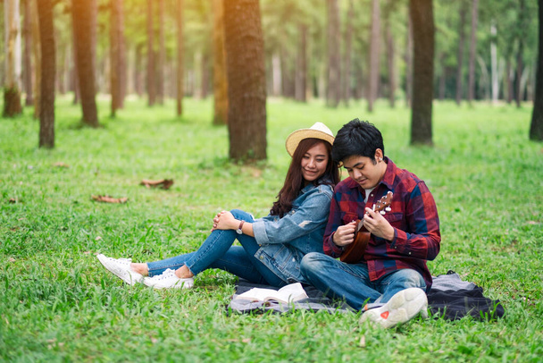 Ein junges Paar spielt Ukulele, während es zusammen im Wald sitzt - Foto, Bild