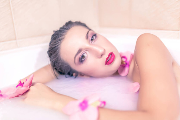 gyönyörű lány pózol egy fürdő tele tejjel és virágokkal fotók - Fotó, kép