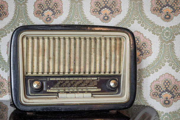 Egy régi tranzisztor rádió, gombokkal és gombokkal a kézi hangoláshoz. A háttérben egy vintage tapéta. Ősi tárgy, az idő elkoptatta és tönkretette.. - Fotó, kép