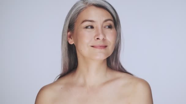 A positive attractive old mature half-naked woman with long gray hair is smiling and laughing isolated over white background in studio - Кадри, відео