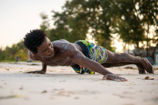 Young Attractive Muscular and Strong Athletic Black African Man at the White Sand Beach Training Archer Push ups Gymnastics Beach Performance - 写真・画像