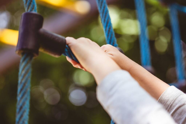 A low angle shot of a child holding on to a blue climbing toy on the playground of a park - Foto, afbeelding