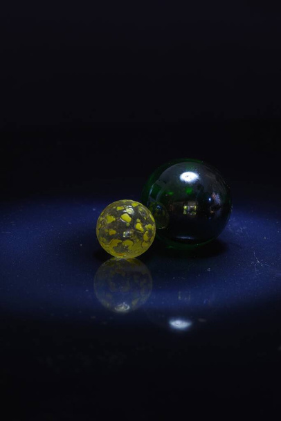 A vertical shot of a black and a yellow transparent marble on a black surface - Foto, imagen