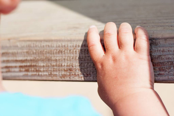 A closeup shot of the cute baby hand on a wooden surface under a sunlight - Foto, Imagem