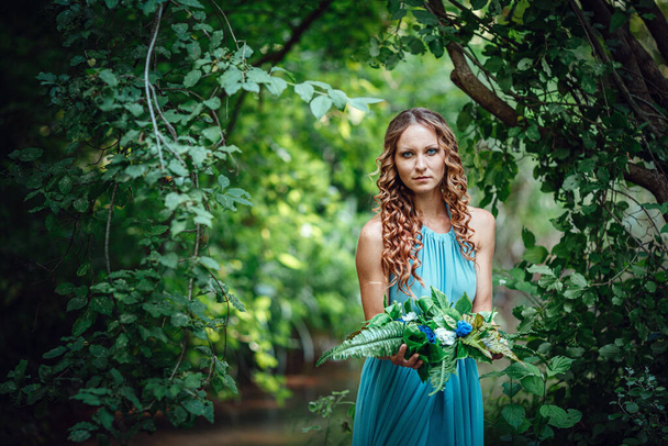 una hermosa joven con el pelo rojo y una corona de flores y helechos en el bosque celebra el Día del Solsticio, a mediados de verano
. - Foto, imagen