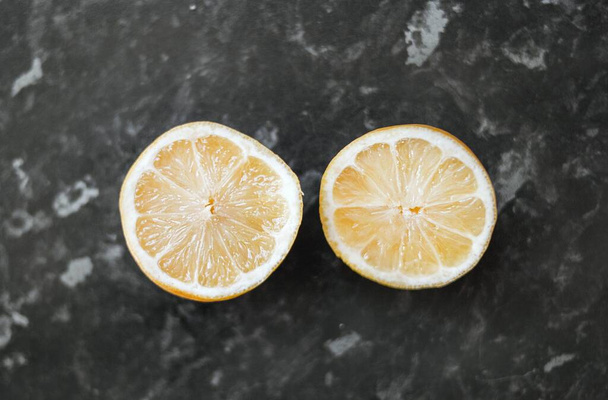 A closeup shot of a cut lemon on a black marble table - Fotoğraf, Görsel