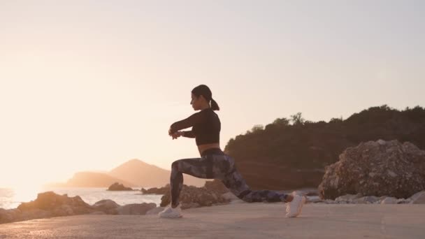 sportowa kobieta jogger rozciągająca się na plaży z widokiem na morze - Materiał filmowy, wideo