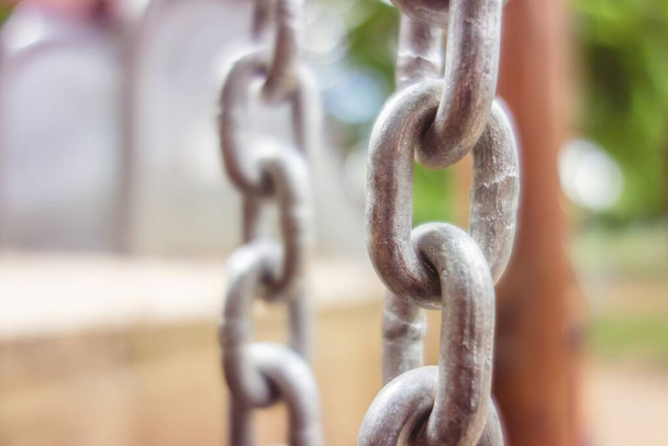 A selective focus shot of the metal chains of a swing set with the trees in the background - 写真・画像