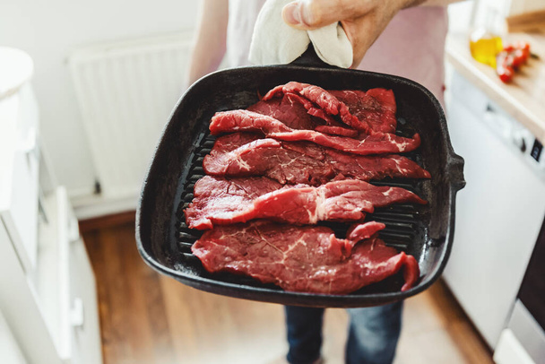 Молодий чоловік готує м'ясо на грилі вдома на кухні
.   - Фото, зображення