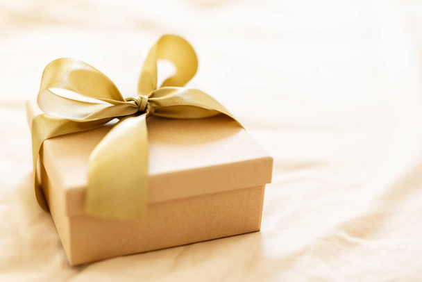 Golden gift with golden ribbon bow on golden background. Closeup.  - 写真・画像
