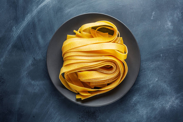Kotitekoinen pasta tagliatelle lautasella tummalla taustalla. Elintarvikkeiden käsite.  - Valokuva, kuva