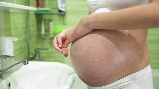 Schwangere schmiert Bauch mit Creme gegen Dehnungsstreifen im Badezimmer - Filmmaterial, Video
