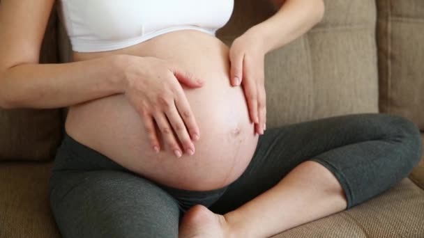 Primer plano de la mujer embarazada acariciando su estómago en el sofá
 - Imágenes, Vídeo