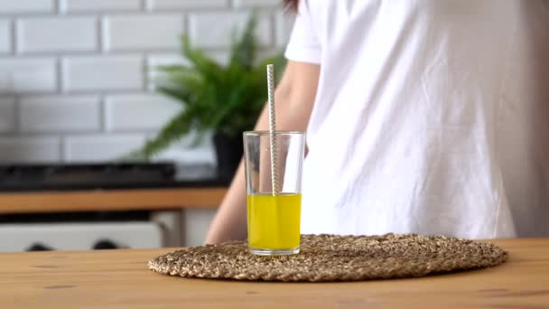 Close up of woman's hand taking glass of lemonade in kitchen. Woman drinking orange soda, quenching her thirst. - Imágenes, Vídeo