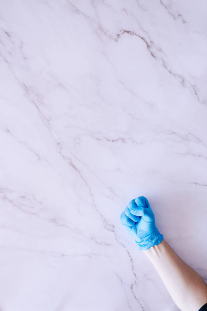 Hand in medical gloves making a fist against a marble background with plenty of copy space - Photo, Image