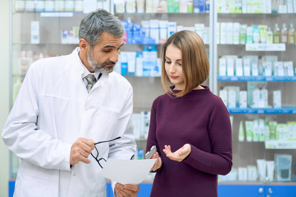 Chemist explaining prescription to woman in drugstore. - 写真・画像
