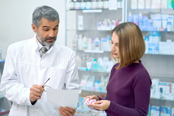 Pharmacist explaining instruction of pills to woman. - 写真・画像