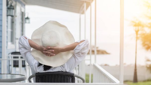 Fiatal lány életmód visel nyári kalap a napsütéses napon pihentető figyelembe könnyű boldogan ül a verandán a tengerparti ház strandon front élvezi az egészséges életminőség nyaralás koncepció - Fotó, kép