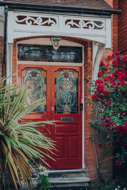 Puerta delantera de vidrieras rojas de una casa eduardiana tradicional en Londres, Reino Unido, enfoque selectivo, enmarcado por árboles y rosas florecientes
. - Foto, Imagen
