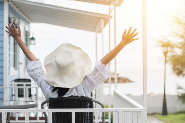 Nyári nyaralás életmód fiatal lány visel naptejes kalap a napsütéses napon pihentető figyelembe könnyedén boldogan ül a verandán a tengerparti ház előtt ünnepli az egészséges élet minőségét - Fotó, kép