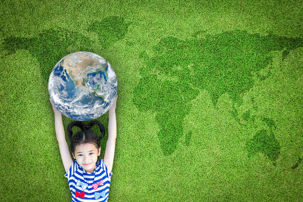 Earth day, ecological friendly and corporate social responsibility concept with kid raising world on green lawn: Element of the image furnished by NASA - Photo, Image