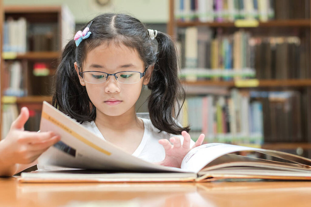 Σχολική εκπαίδευση και αλφαβητισμός έννοια με την ασιατική κορίτσι παιδί μαθητή μάθησης και ανάγνωσης βιβλίο στη βιβλιοθήκη ή την τάξη - Φωτογραφία, εικόνα