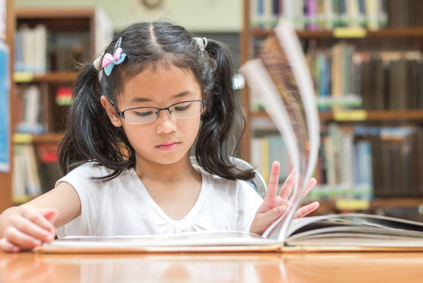 Поняття шкільної освіти та грамотності з азійською дівчинкою-студенткою, яка вчиться і читає книжку в бібліотеці або класі. - Фото, зображення