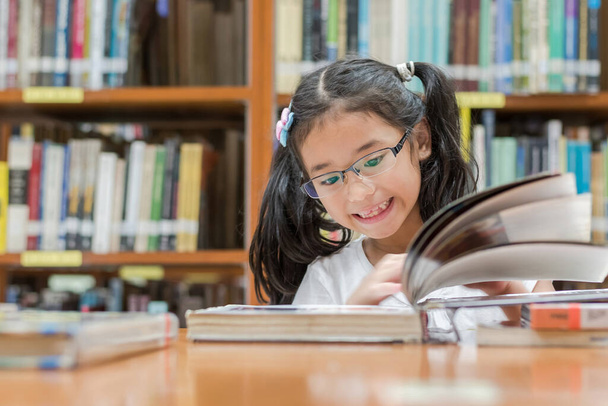 Educación escolar y concepto de alfabetización con niña asiática estudiante de aprendizaje y lectura libro en la biblioteca o el aula - Foto, Imagen