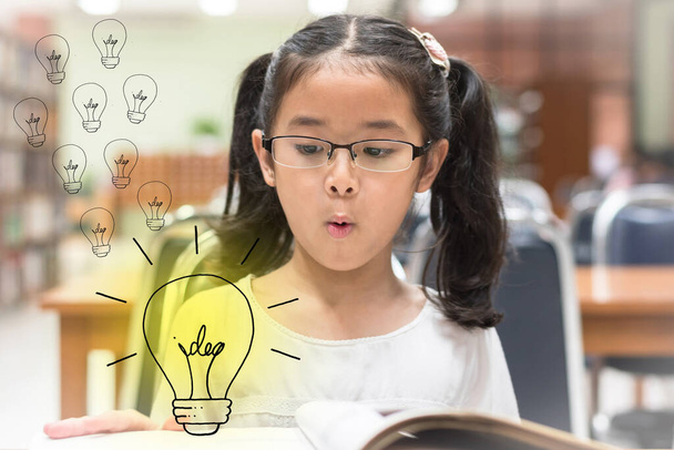 Innovative kreative Idee für Urheberrechtskonzept mit Kind überrascht Lesebuch mit Glühbirne in Bibliothek - Foto, Bild