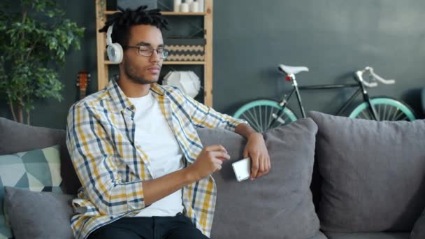 Slow motion of handsome mixed race man enjoying music through headphones holding smartphone - Video