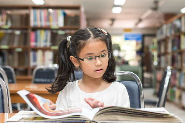 School education and literacy concept with Asian girl kid student learning and reading book in library or classroom - 写真・画像